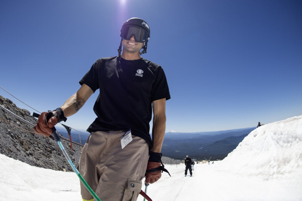 Nick Goepper smiles at the camera while riding the rope tow on a sunny day on snow.